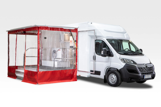 event-truck-ariston Biały samochód eventowy od firmy Bannert z zamontowanym na boku rozkładanym namiotem z przezroczystymi ściankami i czerwonymi elementami. Samochód prezentuje mobilne stoisko wystawowe.