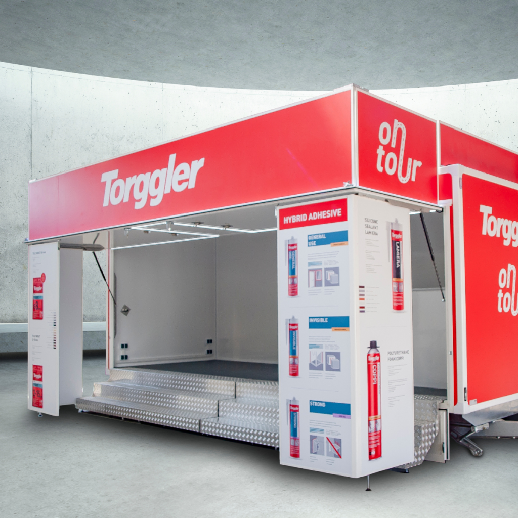 przyczepa-wystawowa-bannert Przyczepa wystawowa Toggler "on tour" w kolorze czerwonym, z rozłożoną sceną i ekspozycją produktów (kleje hybrydowe).