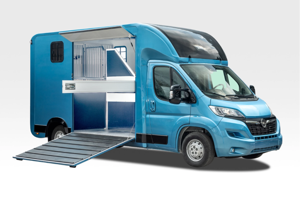 samochod-koniowoz Niebieski koniowóz na bazie samochodu dostawczego, z otwartą klapą i platformą załadunkową do transportu koni.